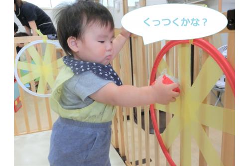 テープとフープで的を作って<br>そこに<span style='color:#ffb770;'>プチプチボール</span>をくっつけて遊びました!<br><br>ボールを手に持ったり、テープを触って<br><span style='color:#ff75ff;'>くっつく感触</span>を楽しんでいると…<br>