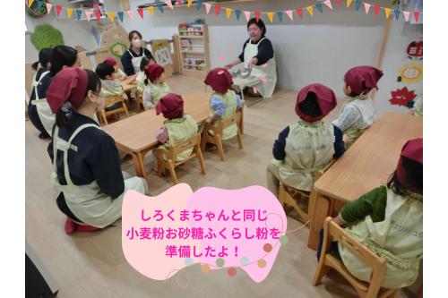 いよいよ<span style='color:#ff007f;'>クッキング</span>のスタート！<br><br>エプロンを着て三角巾をして手も洗って<br><span style='color:#ff7f00;'>準備万端</span>の子どもたち。<br><br>ボウルに入った<span style='color:#007fff;'>「小麦粉、お砂糖、ふくらし粉(ホットケーキミックス)」</span>を<br>紹介すると<span style='color:#ff007f;'>「しろくまちゃんと同じだね」</span>となんだか嬉しそう<span style='color:#ff0000;'>♡</span>